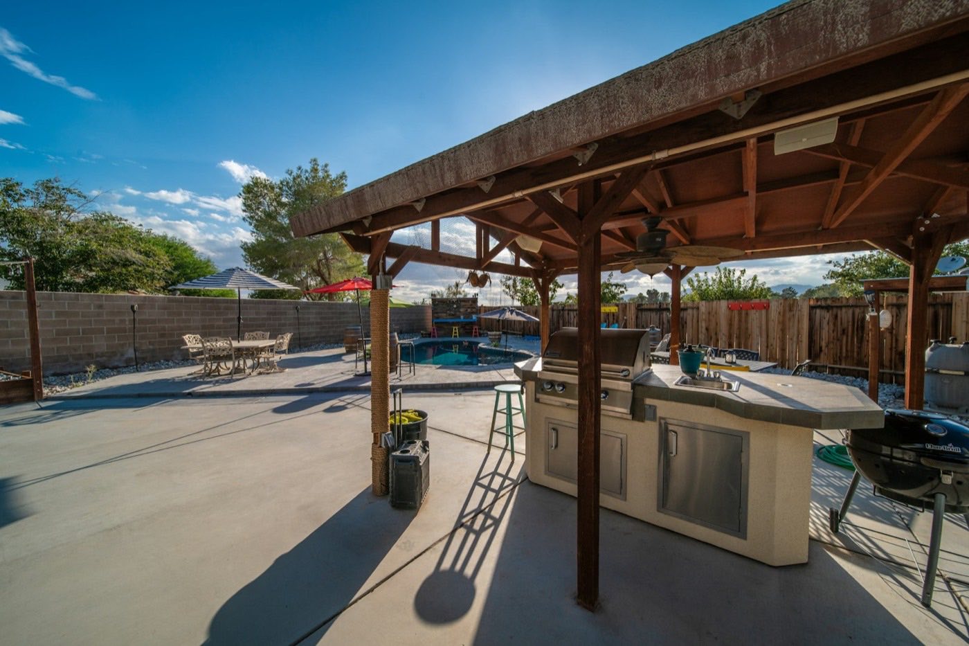 Shaded outdoor kitchen with a built-in grill beside the pool deck.