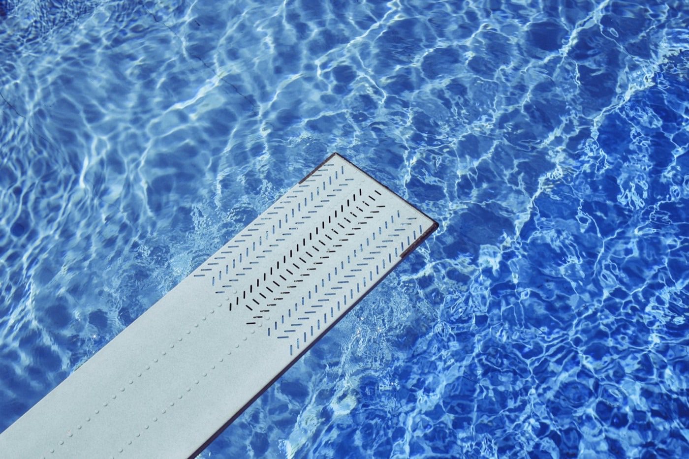 Diving board extending over rippled blue pool water.