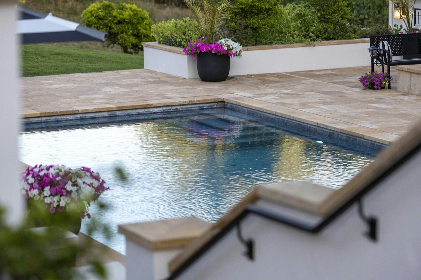 Pool and patio bordered by raised beds of flowering plants.